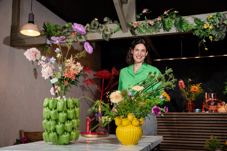 De bloemiste staat in haar atelier tussen aparte vazen met allerlei bloemen in Limburg.