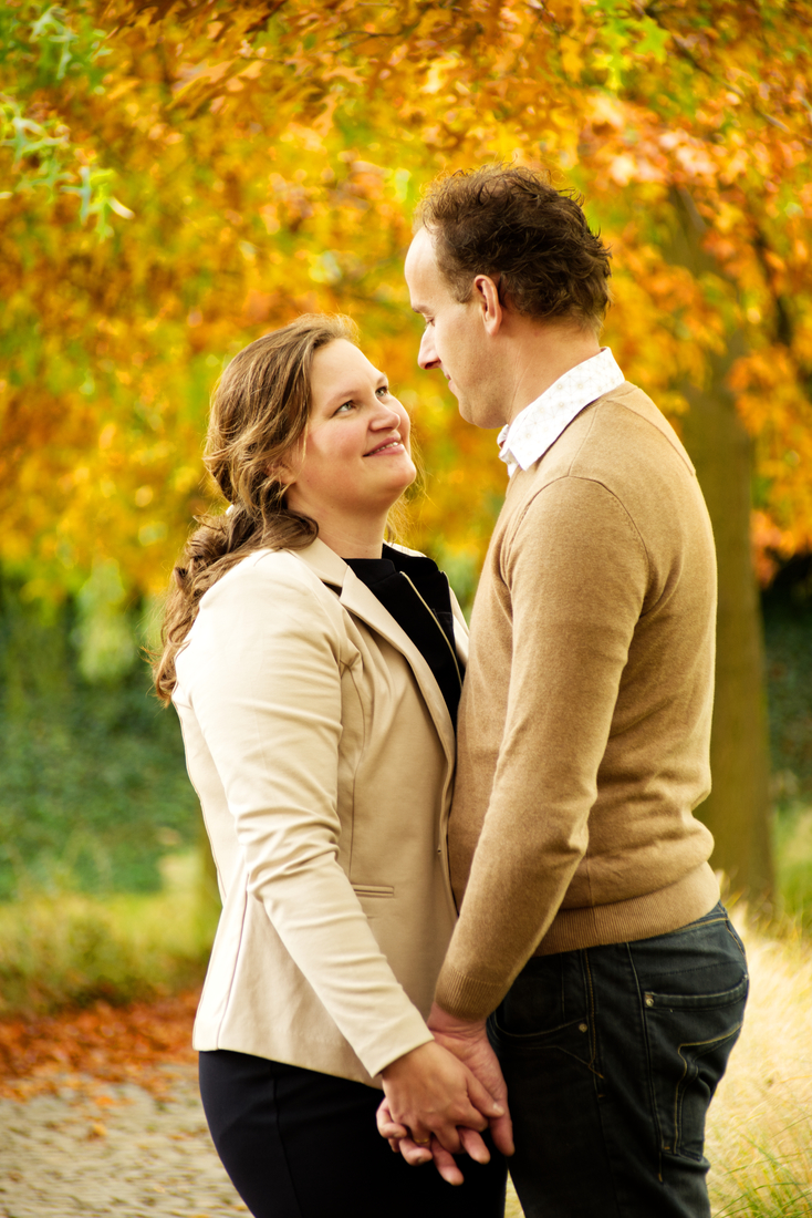 Een echtpaar kijkt verliefd naar elkaar in een park tijdens een herfst fotoshoot met de familie.